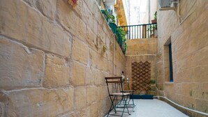 A narrow stone alley with a wooden chair and a table, a small balcony with plants, and a lattice window. - Comfy 2 BR Flat in the Heart of Floriana (Floriana)