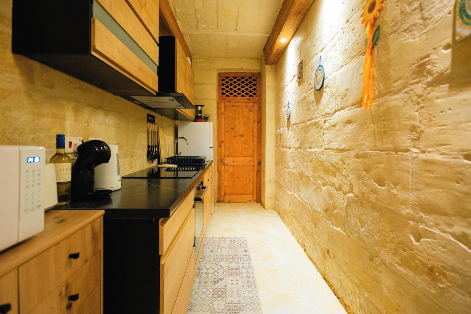A narrow kitchen with wooden cabinets, a black countertop, and a patterned rug.