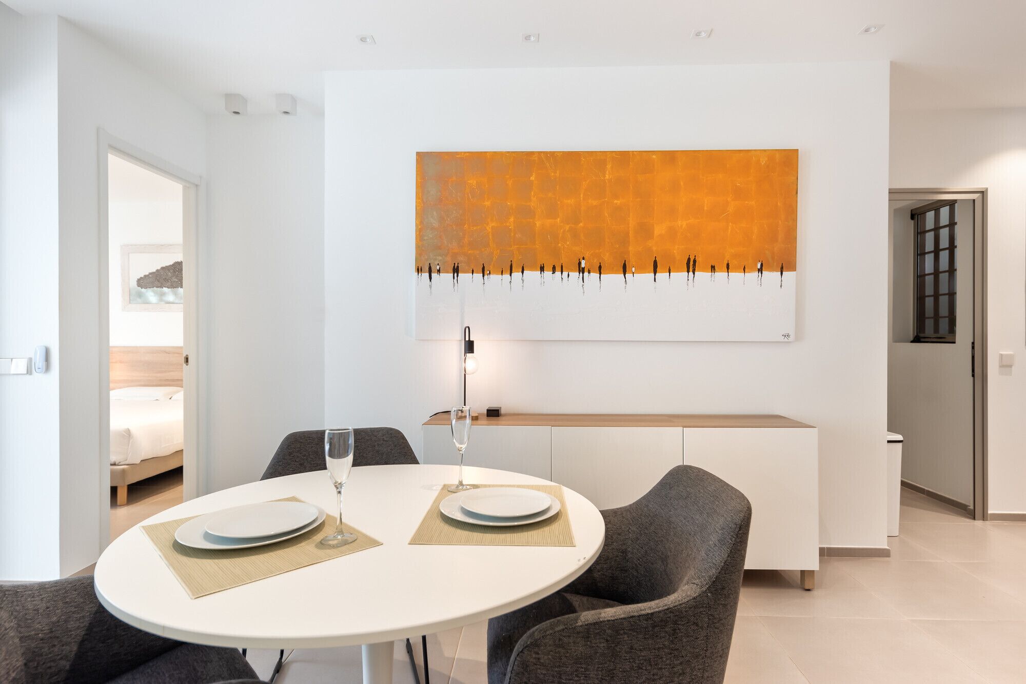 Une chambre d’hôtel moderne dotée d’un coin repas comprenant une table ronde, deux chaises et un grand tableau abstrait placé au-dessus de la table.