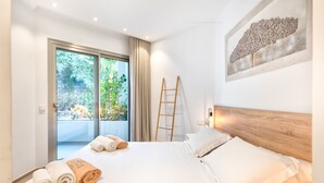 Habitación de hotel con cama, cabecera de madera, escalera y vista a follaje por la ventana.