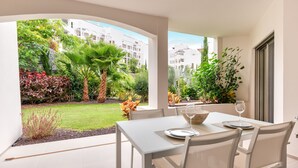 Un comedor con una mesa y sillas, vistas a un jardín con diversas plantas y un edificio al fondo.