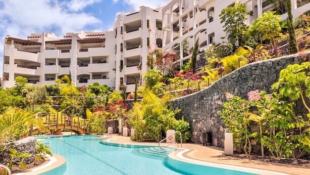 Un resort con piscina, abundante vegetación y un edificio de varios pisos con balcones.