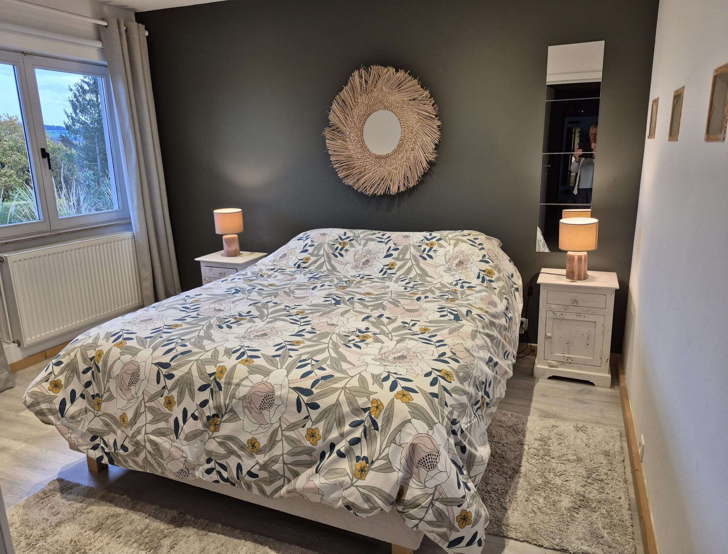 Een slaapkamer met een bed, twee nachtkastjes, een spiegel en uitzicht op het groen.