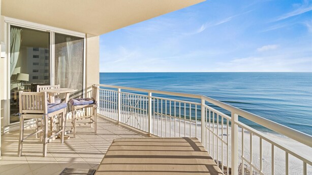 A balcony with a view of the ocean, a table with chairs, and a railing. - Indigo East 1402 (Pensacola)