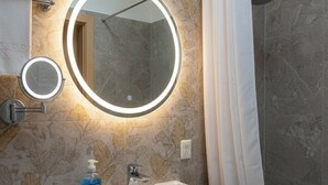 Ein Badezimmer mit einem weißen Waschbecken, zwei runden Spiegeln, einer Handseifenflasche und einer Duschvorhang.