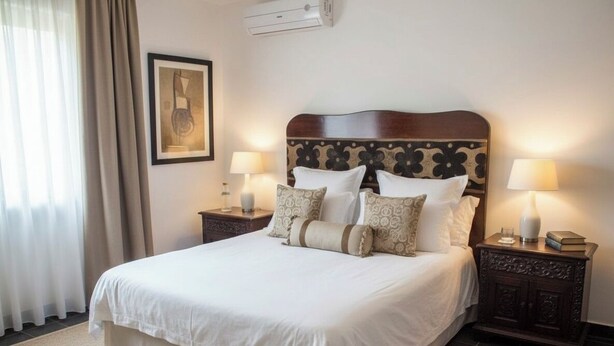 A neatly made bed with white linens and decorative pillows, flanked by two bedside tables with lamps and a framed artwork on the wall. - sherif home la hacienda (Ras Sidr)