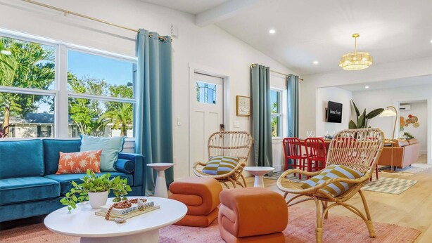 Una sala de estar moderna con un sofá azul, otomanas naranjas, sillas de mimbre y una mesa de centro blanca.