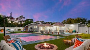 Un patio trasero con una chimenea, mobiliario exterior, piscina y una zona de juegos.
