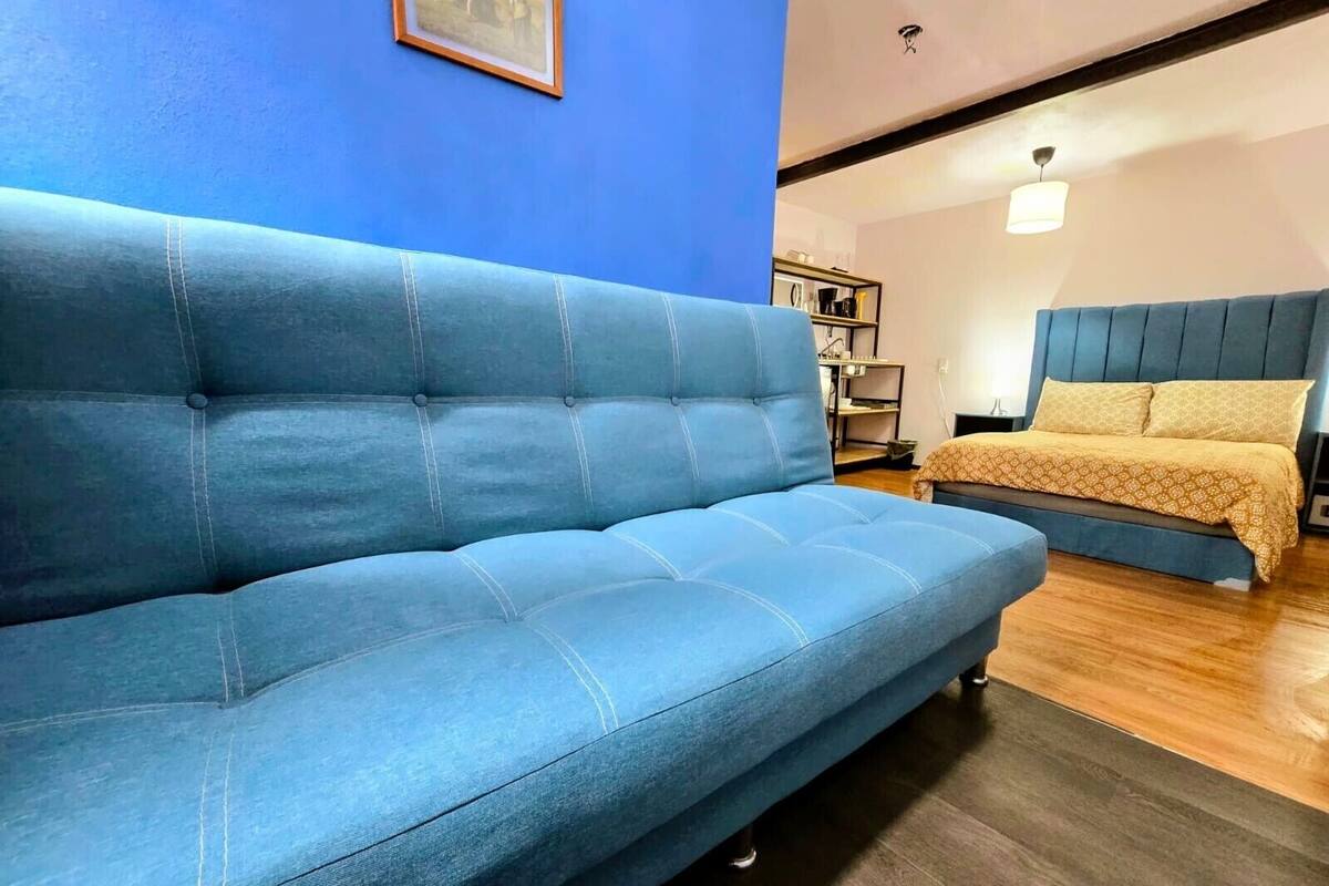 A blue sofa in a room with a bed, wooden flooring, and a blue wall.