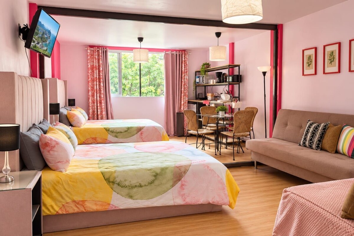 Habitación de hotel con cama, sofá, escritorio, silla, televisor y estantería.