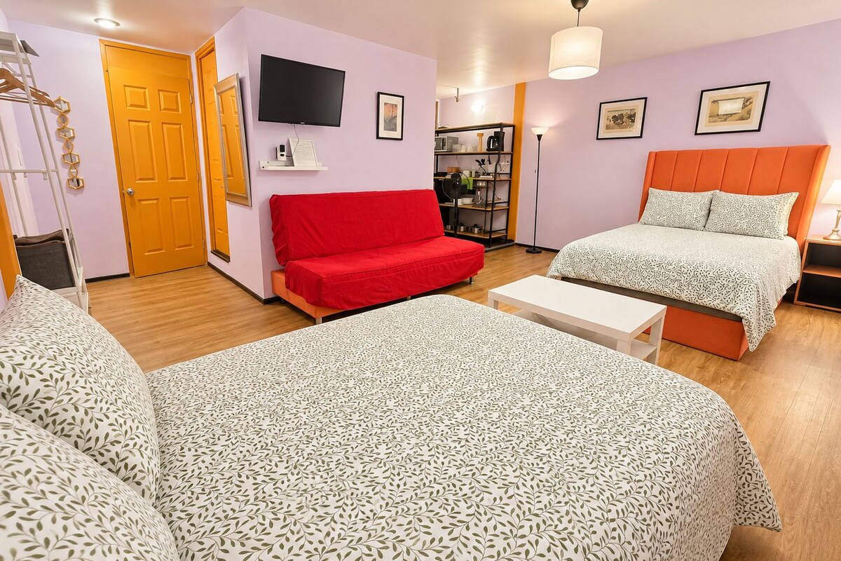 A hotel room with two beds, a red sofa, a TV, a bookshelf, and a desk.