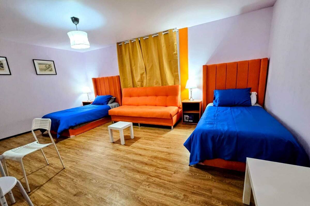 A hotel room with two single beds, a sofa, a small table, and a chair.