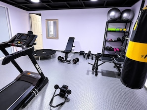 A gym with a treadmill, bench, dumbbells, and a punching bag.