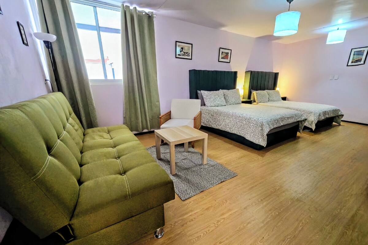 A room with a green sofa, a small table, a bed with a headboard, and a chair.