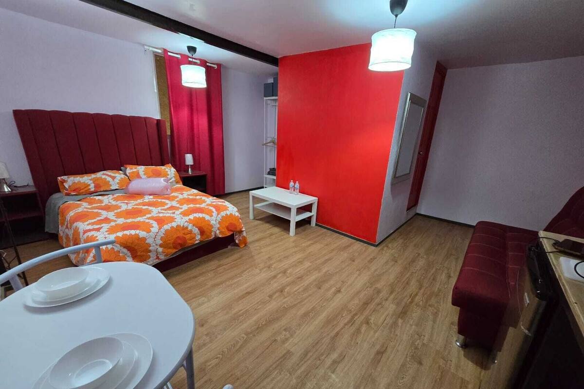 A hotel room with a bed, a small table with plates, a bench, and a red accent wall.