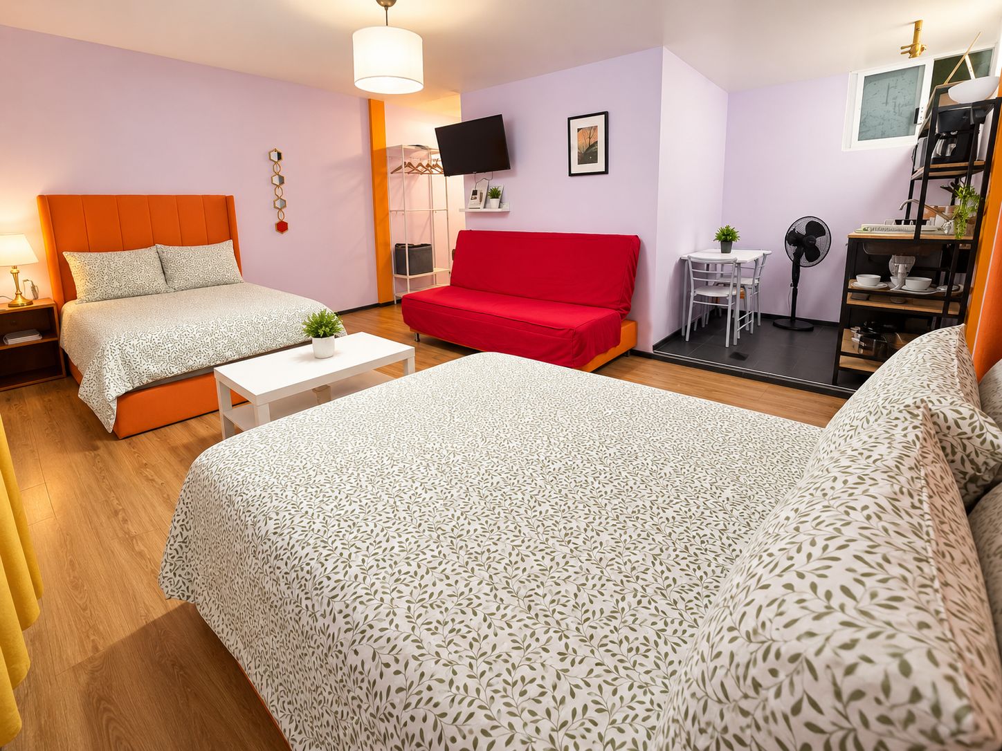 A hotel room with two beds, a red sofa, a small table, a TV, and a desk with a chair.