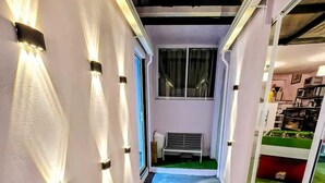 A narrow hallway with a bench, a small garden area with artificial grass, and a billiards table in the background. - CAXA TEGUI (Mexico City)
