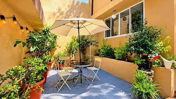An outdoor patio with a table and chairs, surrounded by potted plants and a large umbrella.