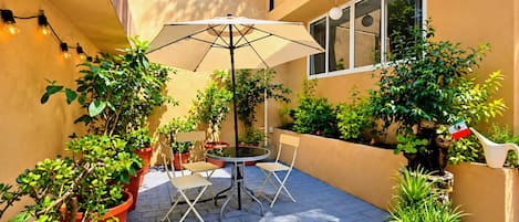 An outdoor patio with a table and chairs, surrounded by potted plants and a large umbrella.
