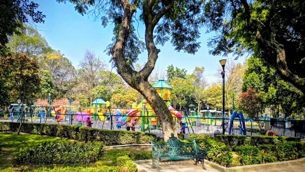 A park with playground equipment, a large tree, and a bench. - CAXA TEGUI (Mexico City)