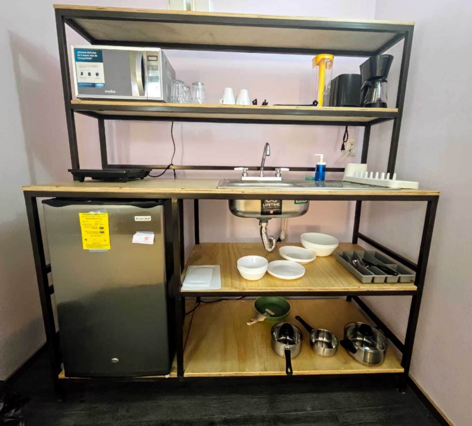A compact kitchenette with a refrigerator, microwave, sink, and various kitchen utensils.