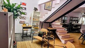 A modern interior with a staircase leading to an upper level, a seating area with wicker chairs, a bookshelf, and a potted plant. - CAXA TEGUI (Mexico City)