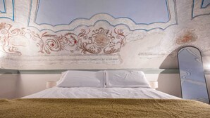Una cama con sábanas blancas, una manta marrón y un techo decorativo con motivos florales.