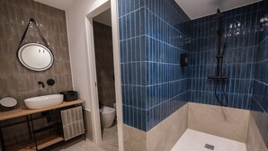 Un baño moderno con un espejo grande, un lavamanos blanco y una zona de ducha con azulejos azules.
