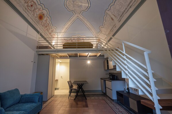 Een ruime woonkamer met een hoge plafond, een trap, een eettafel en een bank.