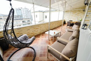 Ein Balkon mit Hängesessel, Sofa und Tisch mit Stühlen.