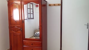 Um guarda-roupa de madeira com espelho, uma pequena mesa de cabeceira e uma cama com colcha xadrez.