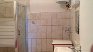 Casa de banho com cabine de chuveiro em vidro, lavatório branco e sanita.
