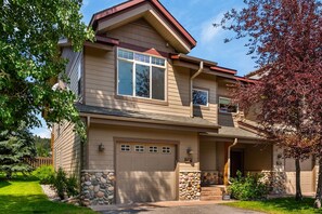 A two-story house with a stone accent wall, a garage, and a covered porch. - Big Sky Townhome | Fireplace + Hot Tub (Big Sky)