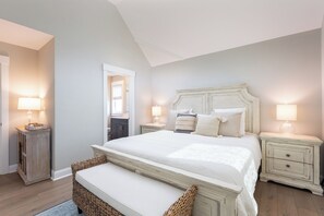 A bedroom with a large bed, two bedside tables with lamps, a wooden bench, and a mirror in the corner. - Ocean-view 4-bedroom, 3.5 bath Corrolla home w/pool+hot tub - sleeps 11 (Corolla)