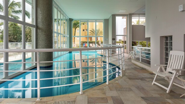 Una piscina interior con suelo de baldosas, barandilla blanca y vistas a palmeras y edificios.