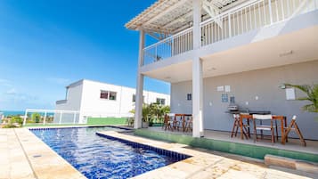 A swimming pool with a patio area, a covered seating area, and a view of the ocean.