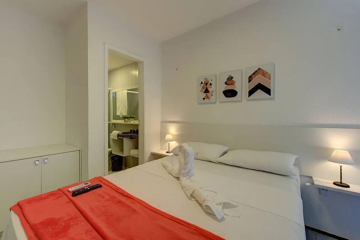 A hotel room with a bed, a nightstand with a lamp, a wardrobe, and a bathroom visible through an open door.