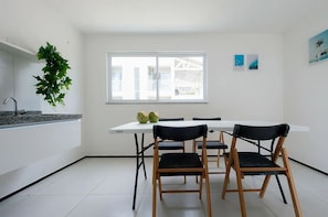 A modern kitchen with a white countertop, two black chairs, a white table, and a window with a view of a building. - Beach Townhouses Triplex Near the Beach By Carpediem (Aquiraz)