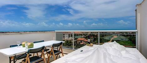 A balcony with a table and chairs, a view of the sea, and a glass partition.