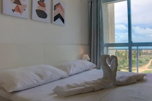 A hotel room with a large bed, white pillows, and a view of a landscape through a large window. - Beach Townhouses Triplex Near the Beach By Carpediem (Aquiraz)