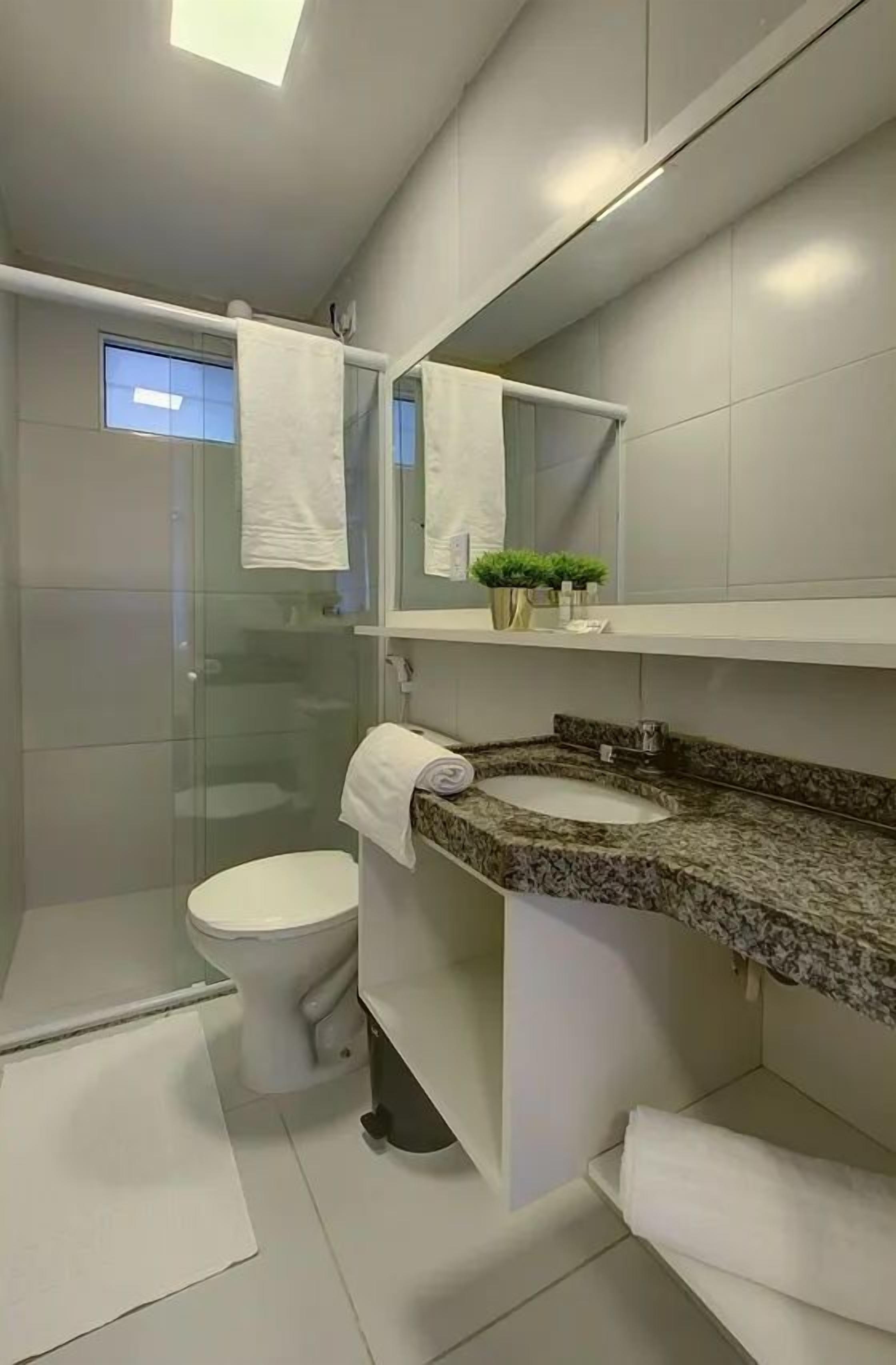 Un baño moderno con cabina de ducha de vidrio, un inodoro, un lavamanos con encimera de granito y un espejo sobre el lavamanos.