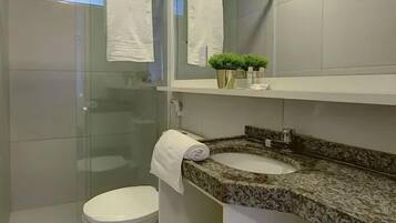 Un baño moderno con cabina de ducha de vidrio, un inodoro, un lavamanos con encimera de granito y un espejo sobre el lavamanos.