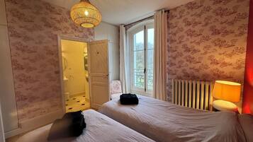 A bedroom with two beds, a hanging light fixture, a window with curtains, and a radiator.