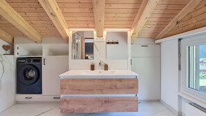 A modern kitchen with a built-in washing machine, wooden ceiling beams, a large window, and a marble floor. - Chez Gredia by Interhome (Täsch)