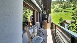 A balcony with wooden chairs, a small table, and a view of a green landscape. - Chez Gredia by Interhome (Täsch)