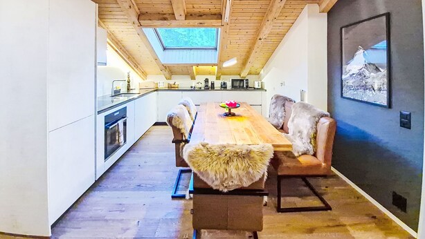 A modern kitchen with wooden beams, a large island, and a dining area with fur-covered chairs. - Chez Gredia by Interhome (Täsch)