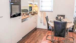 Ett modernt kök med inbyggd ugn, mikrovågsugn och diskmaskin, samt en matplats med bord och stolar.