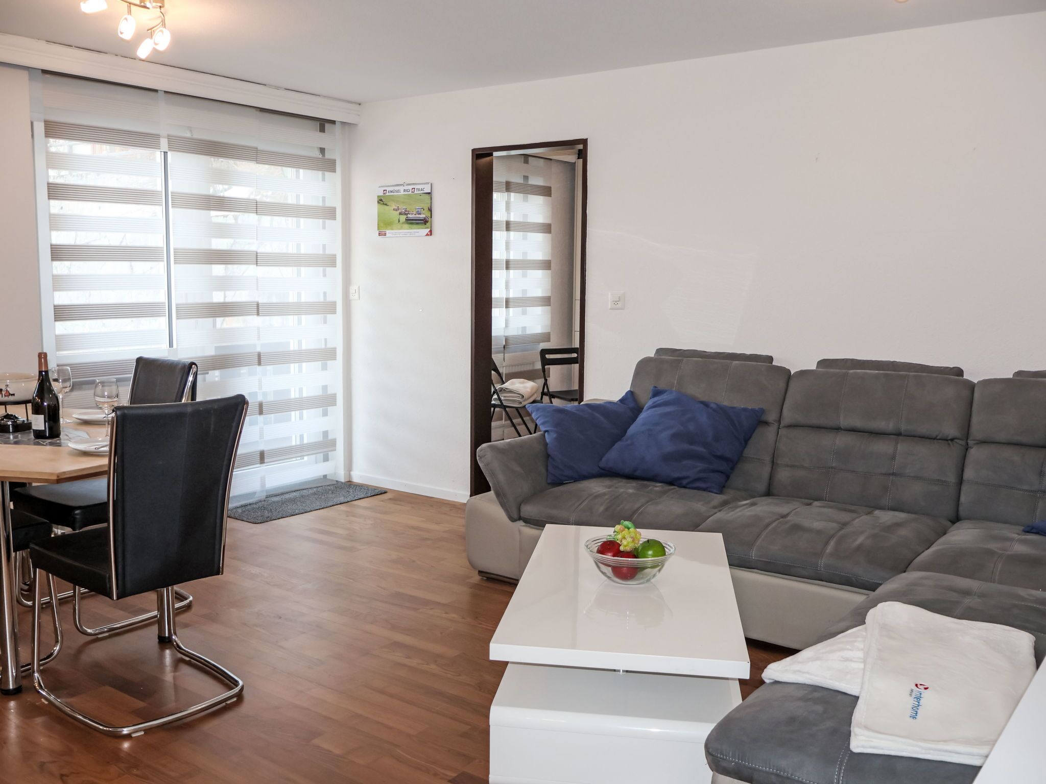Un salon moderne avec un canapé gris, une table à manger avec des chaises et une table basse sur laquelle se trouve un saladier rempli de fruits.