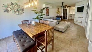 A spacious living area with a wooden dining table, cushioned seating, a sofa, and a television mounted on a white cabinet.