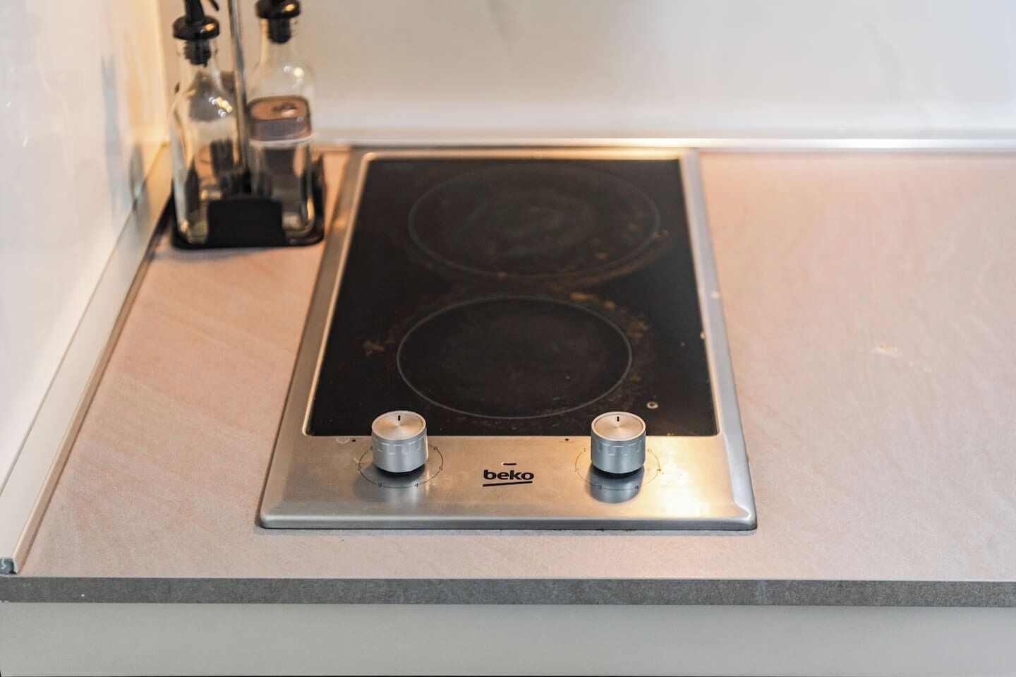 Een keuken met een zwart inductiefornuis en twee knoppen, een fles olie, en een klein zwart apparaat op het aanrecht.